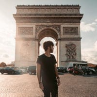 Photo of young man standing in front of Arc de Triomphe in Paris