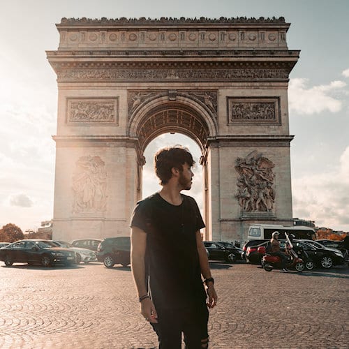 Photo of young man standing in front of Arc de Triomphe in Paris